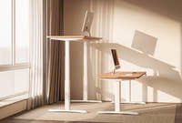 Shappa MO2 electric standing desks at different heights with timber tabletop and white frame, showing sit-stand adjustment in a sunlit home office