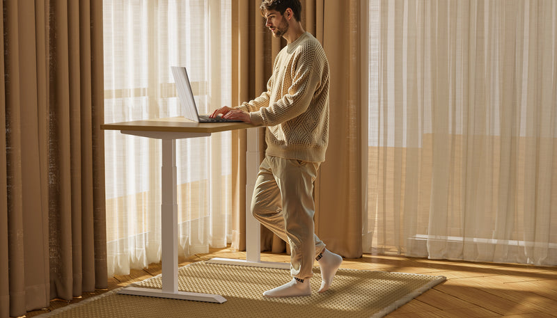 Man working on a laptop at a Shappa MS2 electric standing desk frame in a bright home office