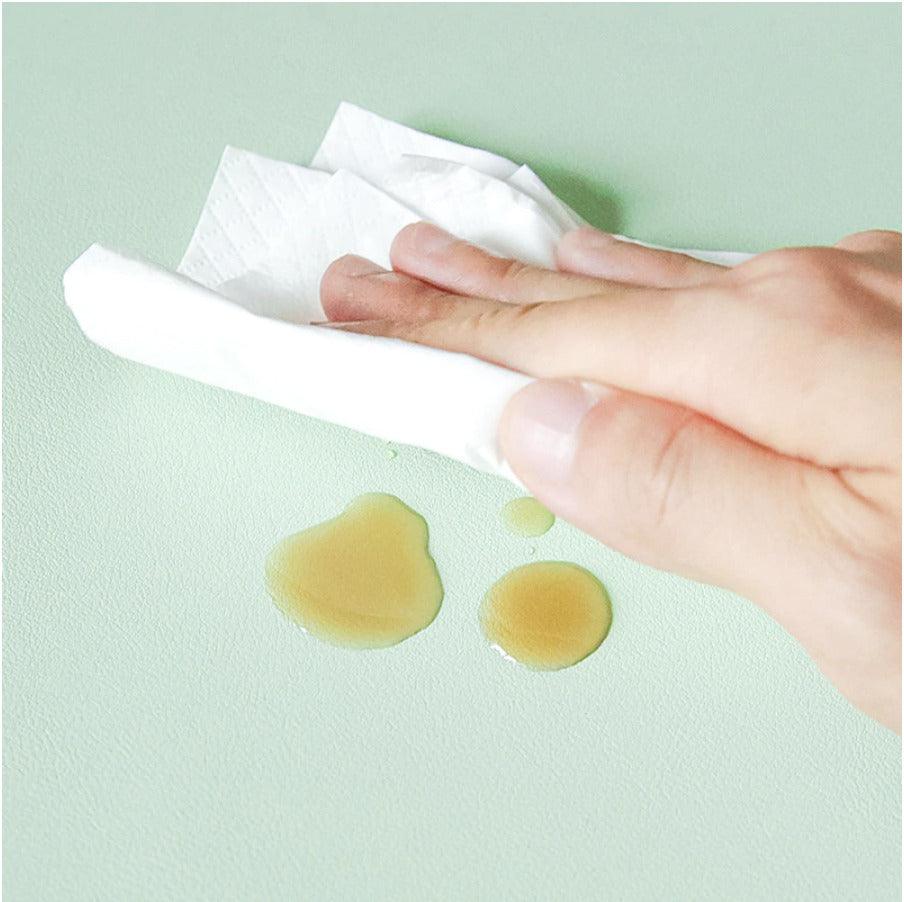 Wiping a spill off the desk mat's waterproof surface with a tissue, demonstrating easy cleaning