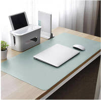Sage green dual-sided desk mat on a wooden desk with a laptop and desk accessories