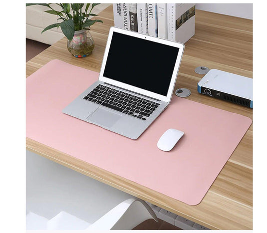 Pink dual-sided desk mat on a home office desk with a laptop, books and a plant
